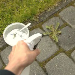 Domowy sposób na chwasty w kostce brukowej: biały proszek w pojemniku i spryskiwacz.