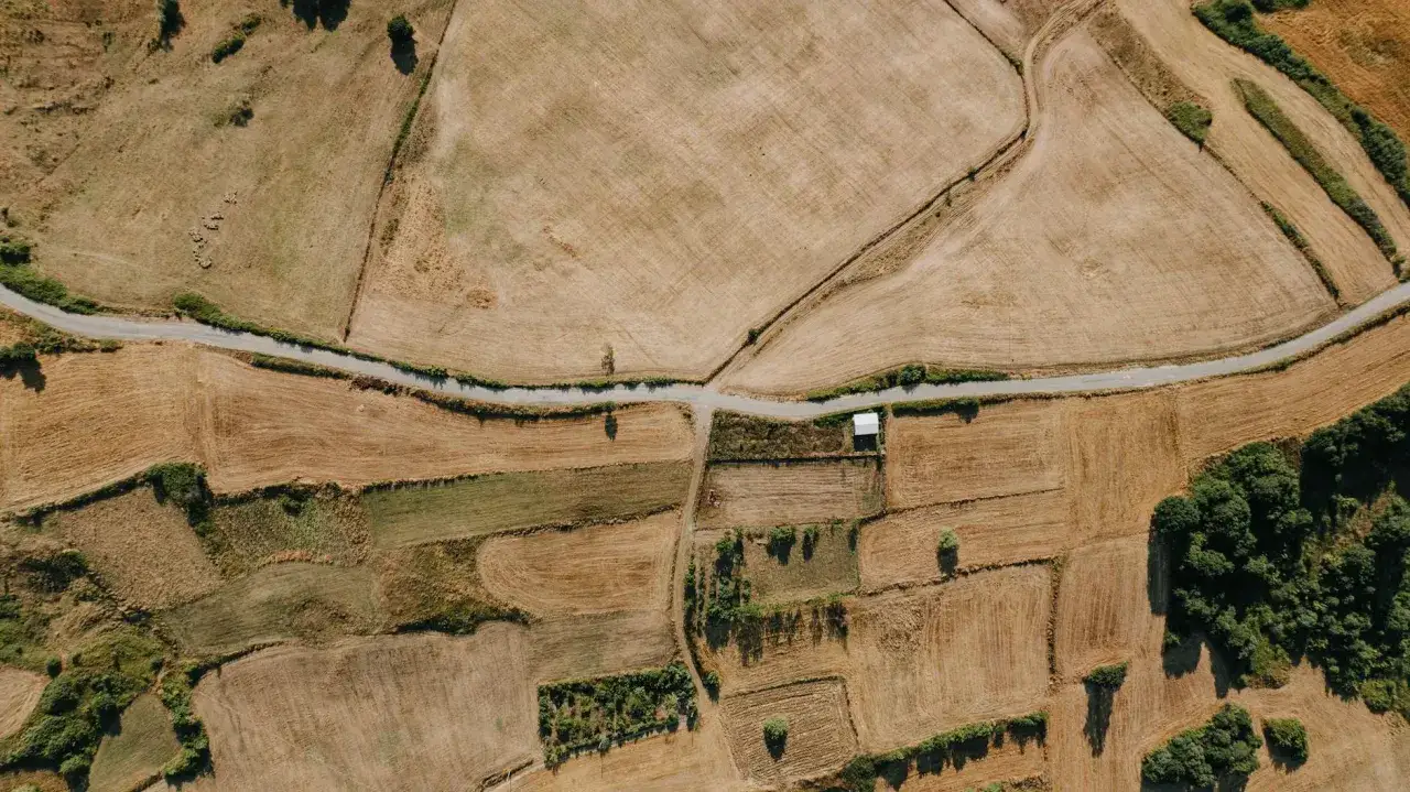 Widok z lotu ptaka na pola uprawne, drogi i mały budynek. Teren wygląda jak jeden wielki hektar przeliczeniowy, podzielony na mniejsze działki.